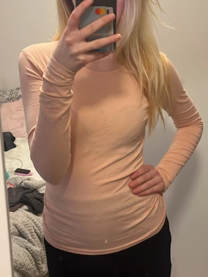 Ljusrosa långärmad topp - En enkel och stilren ljusrosa långärmad topp med rund halsringning. Toppen har en tight passform och är tillverkad i ett mjukt, stretchigt material som sitter skönt mot kroppen. Perfekt att matcha med jeans eller kjol för en clean look.