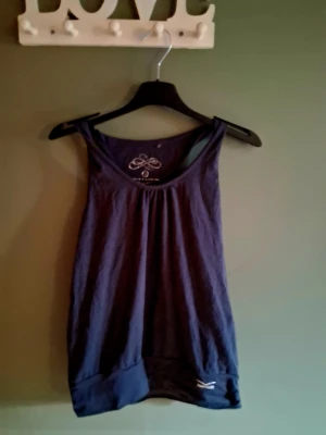 Mörkblå linnetopp med brodyr - Snygg mörkblå linnetopp med broderad detalj i nacken och bredare kant nedtill. Toppen har en avslappnad passform och är tillverkad i mjukt bomullsmaterial. Perfekt för en chill och stilren look.