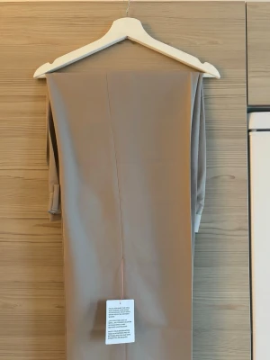 Beige kostymbyxor med pressveck - Helt oanvända beige kostymbyxor med klassiskt rakt ben och pressveck framtill. Byxorna har hög midja och stängs med dragkedja och hake. Helt nya som kommer med lapparna på samt skickas i samma paket som jag fick hem dem i. Strl: W32 & L34.