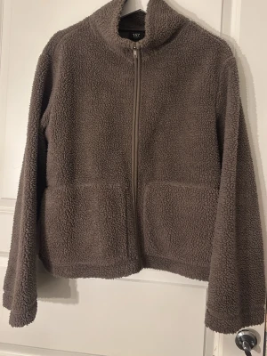 Brun teddyjacka med dragkedja - Mysig brun teddyjacka från 157 , fluffigt material som ger en avslappnad look. Perfekt för kyliga dagar och enkel att matcha med olika outfits.