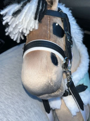 Käpphäst med svartvit man - Säljer en käpphäst med mjuk beige plysch, svart och vit man i garn. Hästen har broderade ögon och mule, samt en fluffig vit kant på täcket. Perfekt för dig som gillar hästar och vill leka eller träna trick.