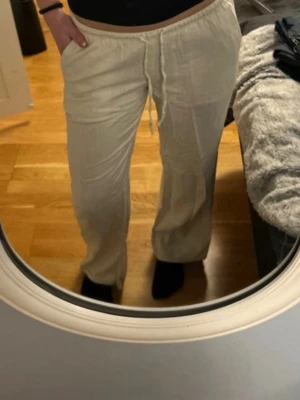Beiga linnebyxor med dragsko - Säljer ett par lågmidjade beiga linnebyxor med avslappnad passform och resår i midjan samt dragsko. Byxorna har raka ben och är tillverkade i ett luftigt linnematerial, perfekta för en chill och stilren look.
