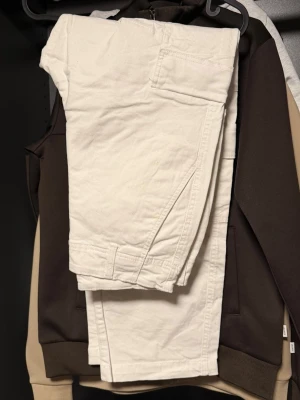 Vita cargobyxor med fickor - Säljer ett par vita cargobyxor med flera praktiska fickor på sidorna. Byxorna har en rak passform och är tillverkade i ett mjukt bomullstyg som känns skönt mot huden. Perfekta för en avslappnad och trendig stil.
