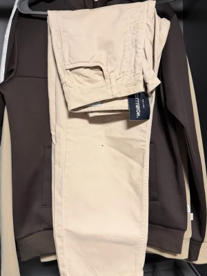 Beige chinos från Morris - Snygga beige chinos från Morris med klassisk rak passform och diskreta fickor. Tillverkade i mjukt bomullstyg som ger en skön känsla och stilren look. Perfekta för dig som vill ha ett par stilrena byxor till garderoben. Storlek: W28 L30