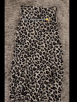 Leopardmönstrad långkjol - Snygg långkjol med leopardmönster i svart och beige. Kjolen har en rak passform och resår i midjan för extra komfort. Perfekt för dig som vill sticka ut med ett djuriskt print.
