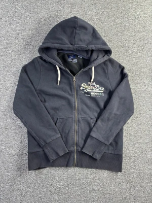 Superdry zip hoodie XS mörkgrå – klassisk modell - Zip hoodie från Superdry i storlek XS. Mörkgrå med tryck framtill och klassisk passform. Perfekt till vardag och streetwear-look.  📏 Storlek: XS 📐 Mått visas i bilderna ✨ Skick: Fint skick – skicket visas i bilderna  Ett bra basplagg som funkar året runt.  💸 Följ mig så får du 10% rabatt på köpet!