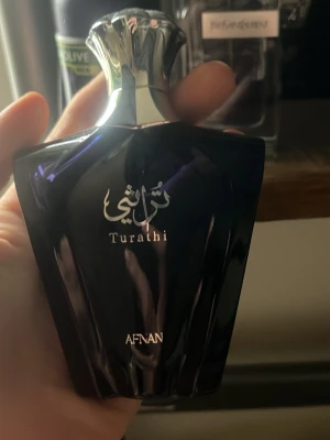 Afnan Turathi parfymflaska - Snygg parfymflaska från Afnan, modell Turathi. Flaskan är mörkblå med silverfärgat lock och har elegant arabisk text på framsidan. Designen är modern och lyxig, perfekt för dig som gillar exklusiva dofter.