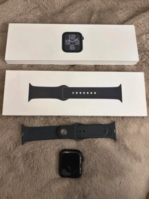 Apple Watch svart aluminium -  Apple Watch i 96%batterihälsa, den svart aluminium med matchande svart silikonarmband. Klockan har en fyrkantig form och digital krona på sidan. Perfekt för dig som vill ha koll på notiser, träning och hälsa direkt på handleden.