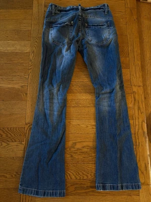 Blå bootcut jeans med slitningar - Säljer ett par blå bootcut jeans med snygga slitningar och tvättade detaljer. Midjemåttet är 34 cm och innerbenslängden är 71 cm.