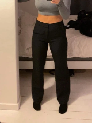 Svarta raka kostymbyxor - Snygga svarta kostymbyxor som är midwaist och raka ben. Klassisk design med pressveck framtill och diskreta fickor. Perfekta för en clean och stilren look. Passar till crop top eller skjorta för en trendig outfit.