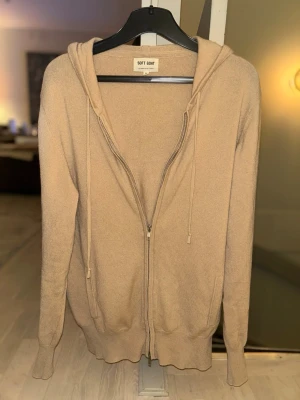 Soft goat zip hoodie  - Snygg beige hoodie från Soft Goat i mjukt material, hel dragkedja framtill och två fickor. Har huva med dragsko och mörkbruna armbågslappar som cool detalj. Perfekt för en avslappnad och stilren look.