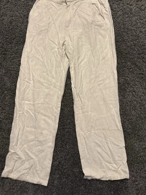 Beiga vida linnebyxor - Säljer ett par beiga linnebyxor med avslappnad passform och raka ben. Byxorna har fickor i sidorna och stängs med dragkedja och knapp. Perfekta för en chill och stilren look. Materialet är lätt och luftigt linne.