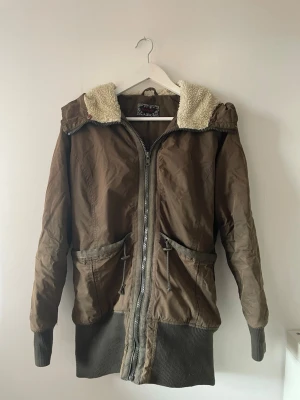 Grön vinterjacka från Havana - Grön vinterjacka från Havana med dragkedja, två stora fickor och mysig fuskpäls i luvan. Jackan har ribbade muddar vid ärmslut och nederkant.