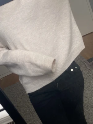 Beige stickad tröja - Mysig beige stickad tröja med rund hals och långa ärmar. Tröjan har en avslappnad passform och ribbade muddar vid ärmslut och nederkant. Perfekt att matcha med jeans för en enkel och stilren look.