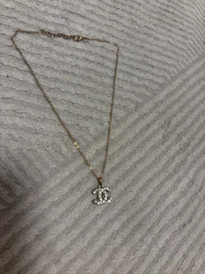 CC halsband  - Snyggt halsband med guldfärgad kedja och ett klassiskt CC-hänge dekorerat med vita stenar. Metallen har svartnat till lite det är därför jag säljer billigt!