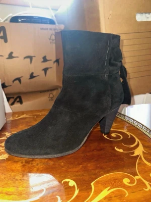 Svarta mockastövletter med rosett - Snygga svarta stövletter i mocka med spetsig tå och medelhög klack. Dragkedja på insidan och dekorativ rosett baktill ger en trendig touch. Perfekta för dig som vill ha en stilren men ändå unik look.