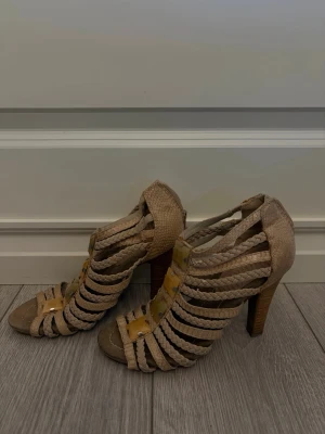 Beige flätade klackade sandaler - Säljer ett par beige sandaler med hög klack och öppen tå. 