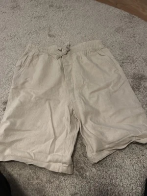 Beige shorts med snörning - Snygga beige shorts med elastisk midja och snörning framtill. Tillverkade i ett mjukt material som känns skönt mot huden. Perfekta för varma dagar och enkel att matcha med olika toppar.