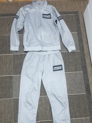 Grå mjukisbyxor från Shan Yes - Snygga grå mjukisbyxor från Shan Yes med tryckt logga på vänster ben. Byxorna har avslappnad passform, resår i midjan och är gjorda i mjukt sweatshirtmaterial. Perfekta för chill dagar eller när du vill ha det bekvämt.