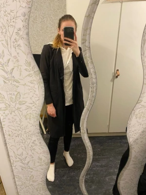Kappa/kavaj - Lång kavaj i fint skick! Kappan har en knapp att stänga med fram samt två fickor fram. Jättefin men tyvärr för liten för mig! Inget fel att anmärka på. Dåliga bilder men den är svart! 