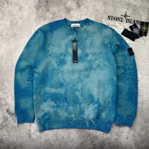 Blå crewneck från Stone Island - (Finns i XS-S-M-L-XL) Säljer en blå crewneck från Stone Island med unikt mönster i olika blå nyanser. Tröjan har rund halsringning, ribbade muddar och klassisk Stone Island-logga på ärmen. Perfekt för dig som gillar streetwear och vill sticka ut.