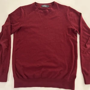 Mörkröd stickad tröja - En enkel och stilren mörkröd stickad tröja med rund halsringning och långa ärmar. Tröjan har ribbade muddar vid ärmslut och nederkant, perfekt för lager på lager och en clean look.