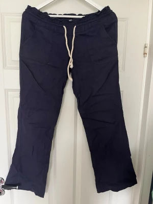 Mörkblå linnebyxor från Roxy - Mörkblå linnebyxor från Roxy med avslappnad passform, resår i midjan och vit dragsko. Byxorna har två fickor fram och är tillverkade i ett svalt linnematerial, perfekta för en chill och ledig stil.💗