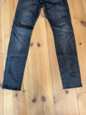 Grå slim fit jeans från G-Star RAW - Säljer ett par grå slim fit jeans från G-Star RAW med klassisk femficksdesign och svarta detaljer på bakfickorna. Jeansen har en snygg tvättad look och raka ben. Perfekta för en avslappnad och trendig stil.