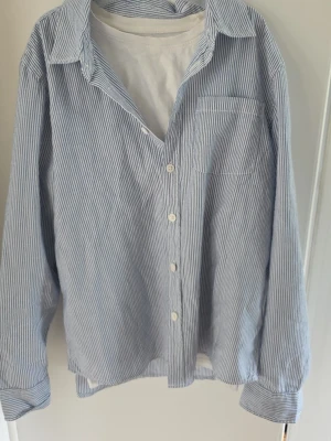 Blårandig skjorta med knappar - Klassisk blårandig skjorta med vit bas och tunna blå ränder. Skjortan har lång ärm, bröstficka och knäppning framtill. Gjord i bommul. 164/Xs. Lite tunnare för sommriga dagar.