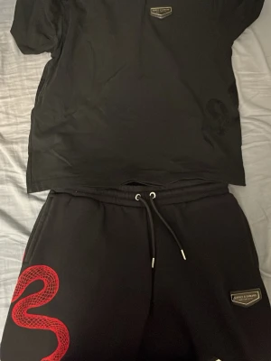 Supply Demand Svarta shorts med röd orm-detalj  - Säljer ett par svarta shorts med en cool röd orm-detalj på ena benet. Shortsen har snörning i midjan för justerbar passform och är tillverkade i ett mjukt material som passar perfekt till sommaren. Pris kan diskuteras vid snabb affär.