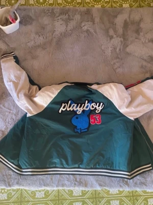 skitsnygg Playboy bomberjacka - Snygg bomberjacka med grönt tyg och vita ärmar. Stor broderad playboy-kanin i blått på ryggen, texten 'playboy' i vitt och siffran 53 i rött. Randiga muddar i svart och vitt. Strl M, säljer pågrund av att jag inte använder den längre ,skriv om frågor💕 Nypris 1200