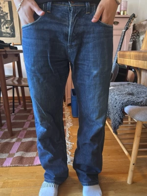 Mörkblå raka wrangler jeans - Säljer ett par mörkblå jeans med rak passform och klassiska fem fickor. Jeansen har kontrastsömmar och är tillverkade i denim. Perfekta för dig som gillar en enkel och tidlös stil.