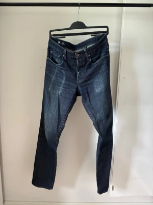 G star 3301 Straight - Snygga mörkblå jeans med slim fit passform och klassisk femficksdesign. Jeansen har lätt slitna detaljer och markerade sömmar, samt en diskret tvättad look framtill och bak. Perfekta för en trendig och avslappnad stil.
