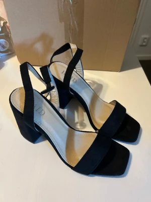 Svarta sandaler med bred klack - Stilrena svarta sandaler med bred klack och öppen tå. Remmar över foten och runt hälen ger en modern look. Klacken är stabil och sulan har en ljus insida. Perfekta för dig som vill ha både stil och komfort till sommaren. Oanvända