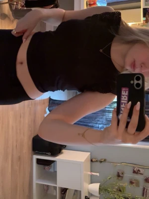 Svart croppad topp med spetsdetalj - Snygg svart croppad topp med spetsdetaljer vid ärmsluten. Toppen har en tajt passform och är tillverkad i ett mjukt, stretchigt material. Perfekt att matcha med höga jeans eller kjol för en trendig look.