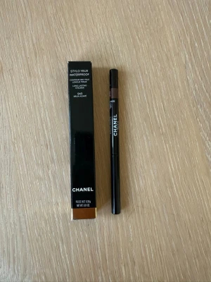 Chanel brun vattenfast eyeliner - Chanel Stylo Yeux Waterproof eyeliner i färgen 943 Brun Agapé. Pennan är smal och svart med en brun spets, och har en elegant design med vit Chanel-logga. Perfekt för precisa linjer och långvarigt resultat. Oanvänd.