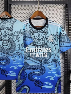 Blå Real Madrid tröja med drakmotiv - Säljer en blå Real Madrid matchtröja från Adidas med ett stort svart drakmotiv över hela framsidan. Tröjan har rund hals med svart kant, korta ärmar och vita detaljer på axlarna. Tryck med 'Emirates Fly Better' på bröstet och klubbmärke på vänster sida.