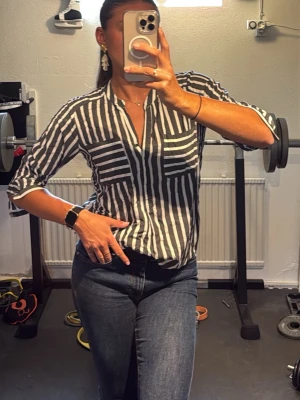 Randig vit grå skjorta - Säljer en snygg mjuk skjorta med gråvita ränder. Skjortan har knappar framtill och trekvartsärm. Perfekt till jeans eller ett par shorts eller bara att slängs över bikinin. Passar även S