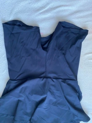 Svart baddräkt med kjoldetalj - Stilren svart baddräkt med v-ringning och kjoldetalj nedtill. Tillverkad i stretchigt material som passar perfekt för simning eller strandhäng. Klassisk och enkel design utan synligt märke.