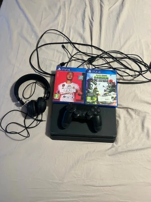 PlayStation 4 med spel och tillbehör - Säljer en svart PlayStation 4 med en matchande svart handkontroll, headset och kablar. Två PS4-spel medföljer: FIFA 20 och Plants vs Zombies Garden Warfare. Perfekt för gamingkvällar med vänner eller soloäventyr.