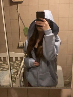 Ljusblå hoodie med nalletryck - Säljer en ljusblå hoodie med dragkedja och huva, även dragkedja runt huvan. Hoodien har flera tryck med en tecknad nalle på bröstet, ryggen, huvan och ärmarna. Mjuk insida och ribbade muddar vid ärmslut och nederkant. Perfekt för en chill och avslappnad stil.