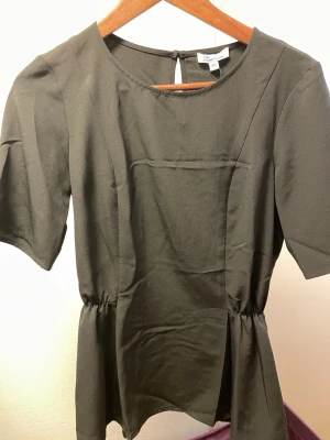 Svart Medusa blus från Pieces - Stilren svart blus från Pieces, modell Medusa. Blusen har rund halsringning, korta ärmar och ett lätt glansigt tyg som ger en elegant känsla. Midjan är lätt rynkad för en snygg siluett. Perfekt att matcha med både jeans och kjol. Prislapp kvar på 399. 