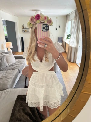 Meet me there x Filippa  - Söt vit kortklänning med omlott och spetsdetaljer. Klänningen har puffiga korta ärmar, volangkant och öppen rygg. Tillverkad i ett lätt material, perfekt för sommarens alla tillfällen. V-ringad och med fina broderade detaljer.