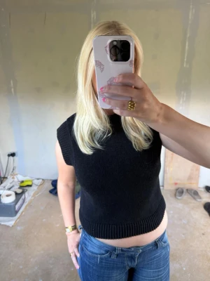 Svart stickad ärmlös topp - Säljer en svart stickad ärmlös topp med ribbade kanter vid hals, ärmhål och nederkant. Perfekt att styla över en skjorta eller t-shirt för en trendig lager-på-lager-look eller ha enskild till ett par snygga jeans🩷