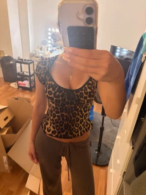 Leopardmönstrad topp med rosett - Snygg leopardmönstrad topp med korta puffärmar och söt rosettdetalj framtill. Toppen har en djup, rundad urringning och är lätt transparent. Perfekt för dig som vill sticka ut lite extra. Materialet känns som tunn polyester.