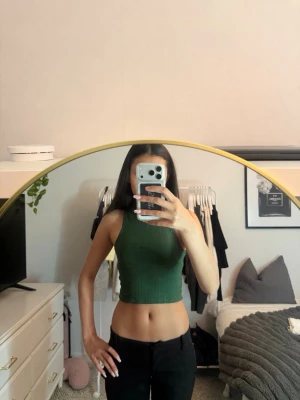 Grön ribbad croppad polotopp - Snygg grön croppad polotopp med ribbad struktur. Toppen är ärmlös och har en hög hals som ger en trendig look. Perfekt att matcha med höga jeans eller kjol för en stilren outfit.