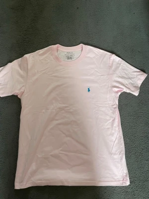 Ljusrosa t-shirt från Polo Ralph Lauren - Snygg ljusrosa t-shirt från Polo Ralph Lauren med blå broderad logga på bröstet. Modellen är slim fit och har klassisk rund hals och korta ärmar. Tillverkad i 100% bomull för en skön och luftig känsla.