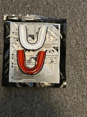 Röd och vit tandskydd - Säljer ett set med två tandskydd i U-form, ett i rött och ett i vitt. Perfekt för sporter som boxning, hockey eller MMA. Tillverkade i plastmaterial och enkla att forma efter tänderna med hjälp av varmt vatten. Instruktioner för anpassning medföljer.