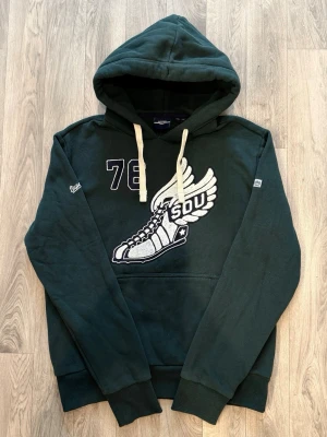 Superdry Hoodie Mörkgrön Strl XL - Superdry mörkgrön hoodie i tjock bomull med klassisk passform som passar rymlig L eller normal XL, storlek XL, bröstvidd 60,5 cm, axelbredd 53 cm, armlängd 70 cm, midja 50 cm, längd 69 cm, i mycket fint skick/nyskick utan synliga tecken på användning.