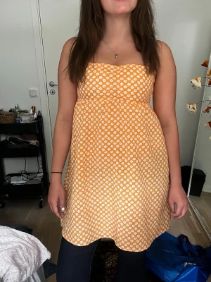 Orange blommig klänning från Divided - Söt orange klänning från Divided med vita små blommor. Klänningen har en rak, ärmlös modell med markerad midja och lätt utställd kjol. Perfekt för sommarens alla tillfällen och ger en fräsch och ungdomlig look.